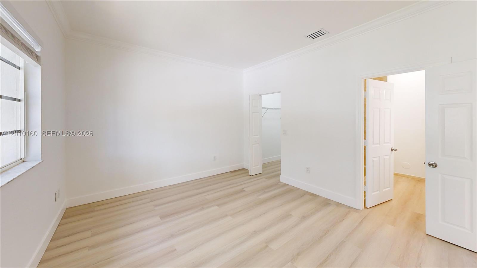 An empty bedroom features white walls, light wood-look flooring, a window, and two doorways — 372 NE 26th Pl # 201, Homestead FL 33033, HOMESTEAD, FL