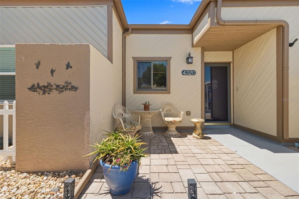 A paved patio area features two wicker chairs, a small table, and a potted plant — 4320 FERN GLEN ST, HOLIDAY, FL