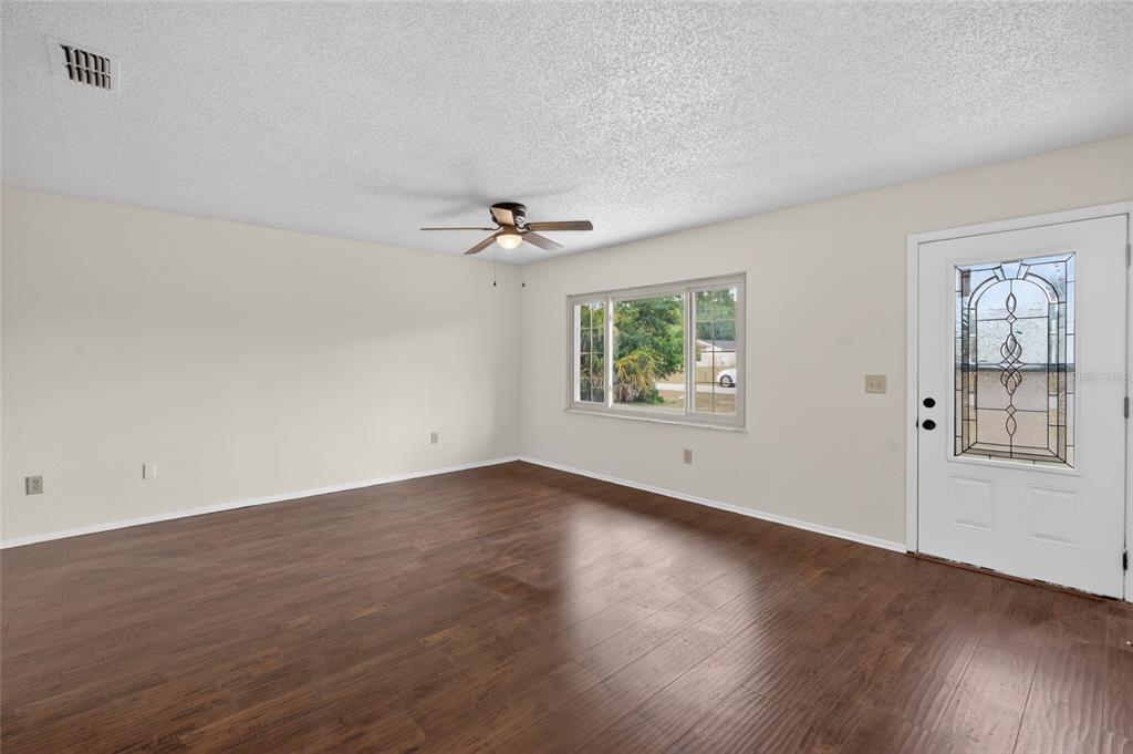 An empty living room features wood-look flooring, a ceiling fan, and a front entry door — 329 OAK TRACK DRIVE, OCALA, FL