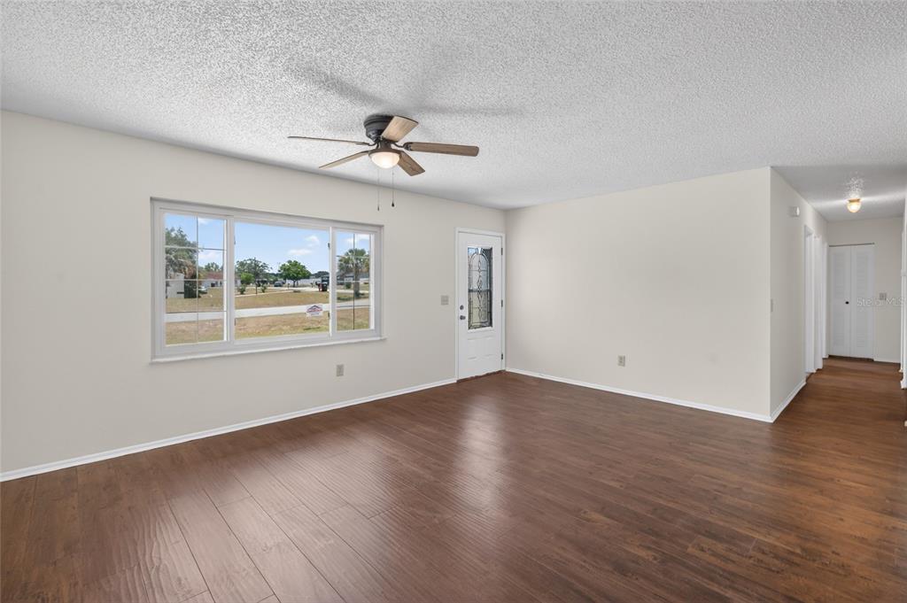 A living room with wood-look flooring, a ceiling fan, and a large window — 329 OAK TRACK DRIVE, OCALA, FL