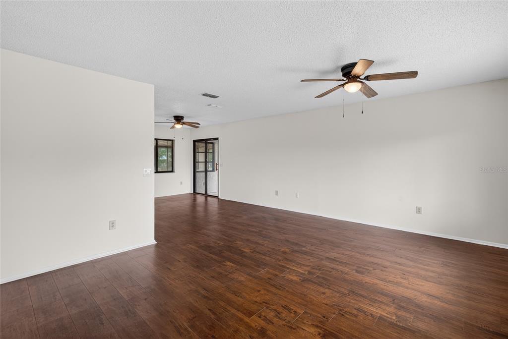 An empty living area features dark wood-look flooring, white walls, and two ceiling fans — 329 OAK TRACK DRIVE, OCALA, FL