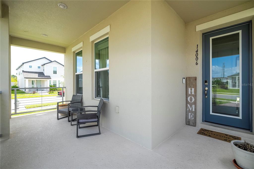 A covered front porch features two wicker chairs, a blue front door, and a welcome mat — 14006 FRASIER STREET, WINTER GARDEN, FL