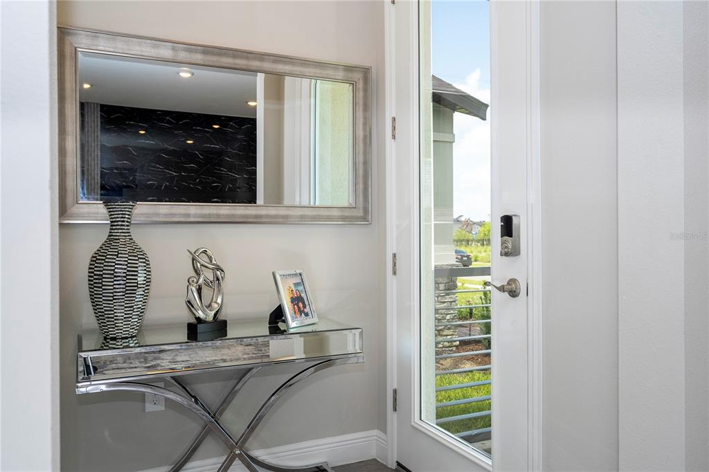 An entryway features a mirrored console table, a wall mirror, and a glass-paneled front door — 14006 FRASIER STREET, WINTER GARDEN, FL
