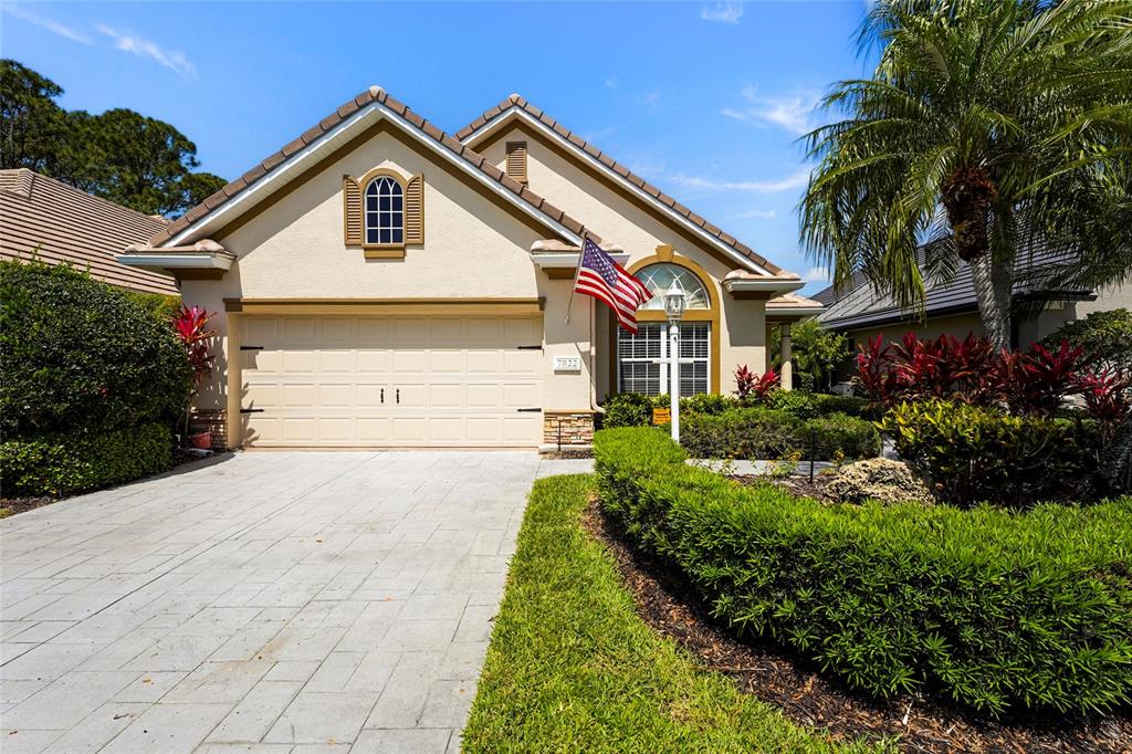 A single-story house with a beige stucco exterior, a two-car garage, and a manicured hedge — 7822 TROON COURT, LAKEWOOD RANCH, FL
