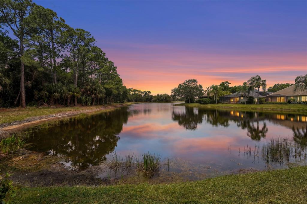 A calm pond reflects a colorful sunset with trees on the left and houses nearby — 7822 TROON COURT, LAKEWOOD RANCH, FL