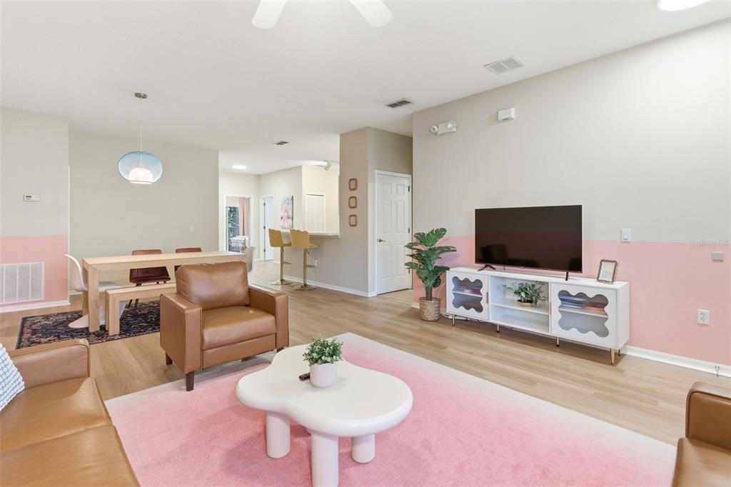 An open-concept living and dining area features pink wall accents, light wood flooring, and furniture — 3119 SUN LAKE COURT UNIT B, KISSIMMEE, FL