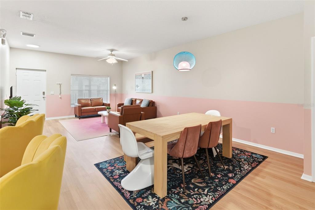 An open-concept living and dining area features light wood floors, pink wall accents, and furniture — 3119 SUN LAKE COURT UNIT B, KISSIMMEE, FL