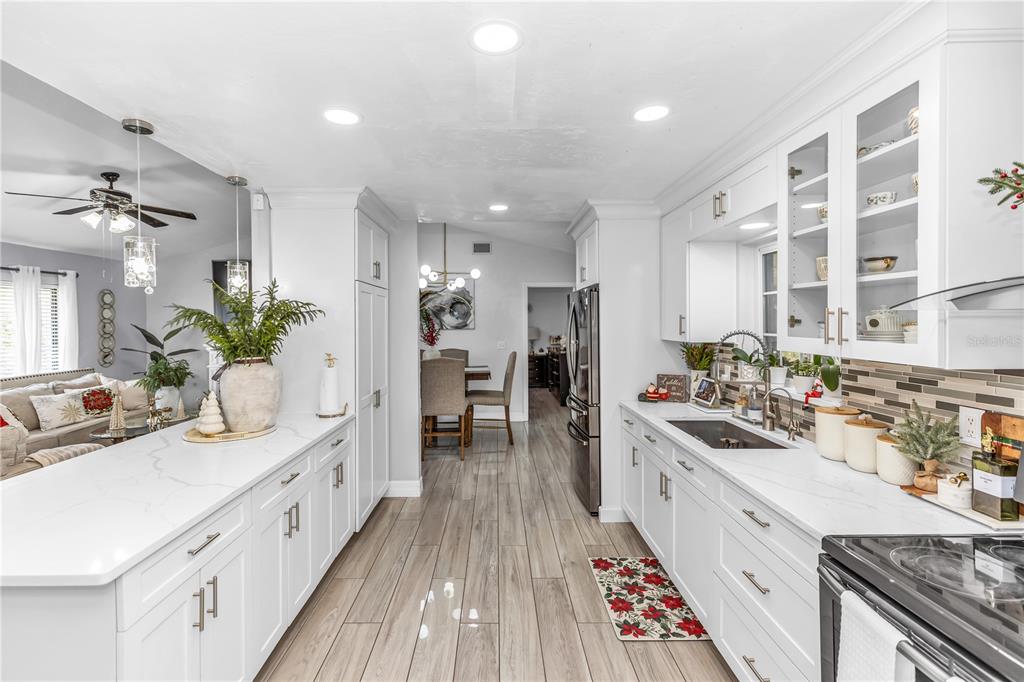 A modern white kitchen features quartz countertops, stainless steel appliances, and wood-look tile flooring — 1390 SAN CARLOS AVENUE, DELTONA, FL