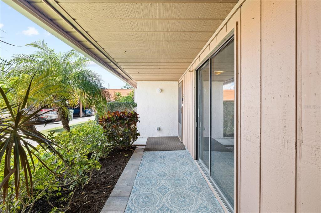 A covered outdoor patio features a patterned rug, sliding glass doors, and adjacent landscaping — 6535 DRAW LANE UNIT 85, SARASOTA, FL