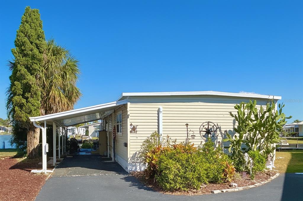 A light-colored mobile home features a side carport, a driveway, and landscaping with a cactus — 144 AMERICANA COURT NE UNIT 218, ST PETERSBURG, FL