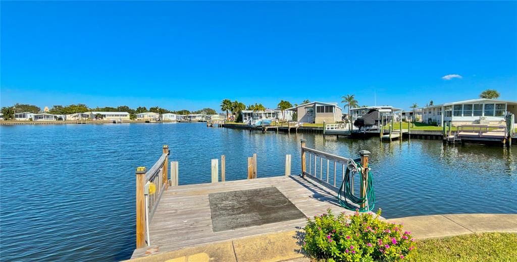 A wooden dock extends into a canal lined with manufactured homes and private boat slips — 144 AMERICANA COURT NE UNIT 218, ST PETERSBURG, FL