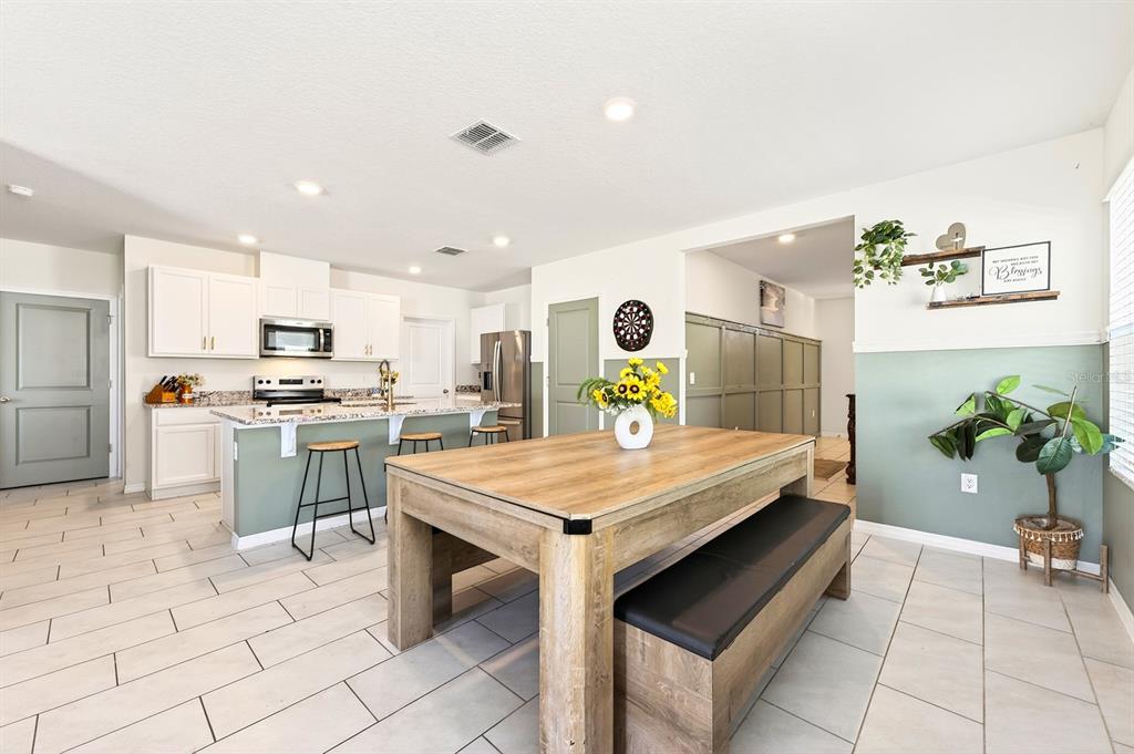 A kitchen with white cabinets, a wooden dining table, and green accent walls — 182 AMBERWOOD WAY, UMATILLA, FL