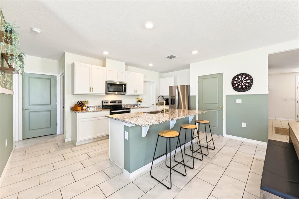 A kitchen features white cabinets, granite countertops, a central island with stools, and green doors — 182 AMBERWOOD WAY, UMATILLA, FL