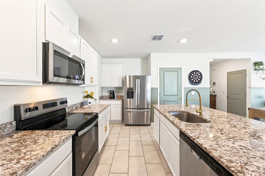 A kitchen features white cabinets, granite countertops, stainless steel appliances, and a central island — 182 AMBERWOOD WAY, UMATILLA, FL