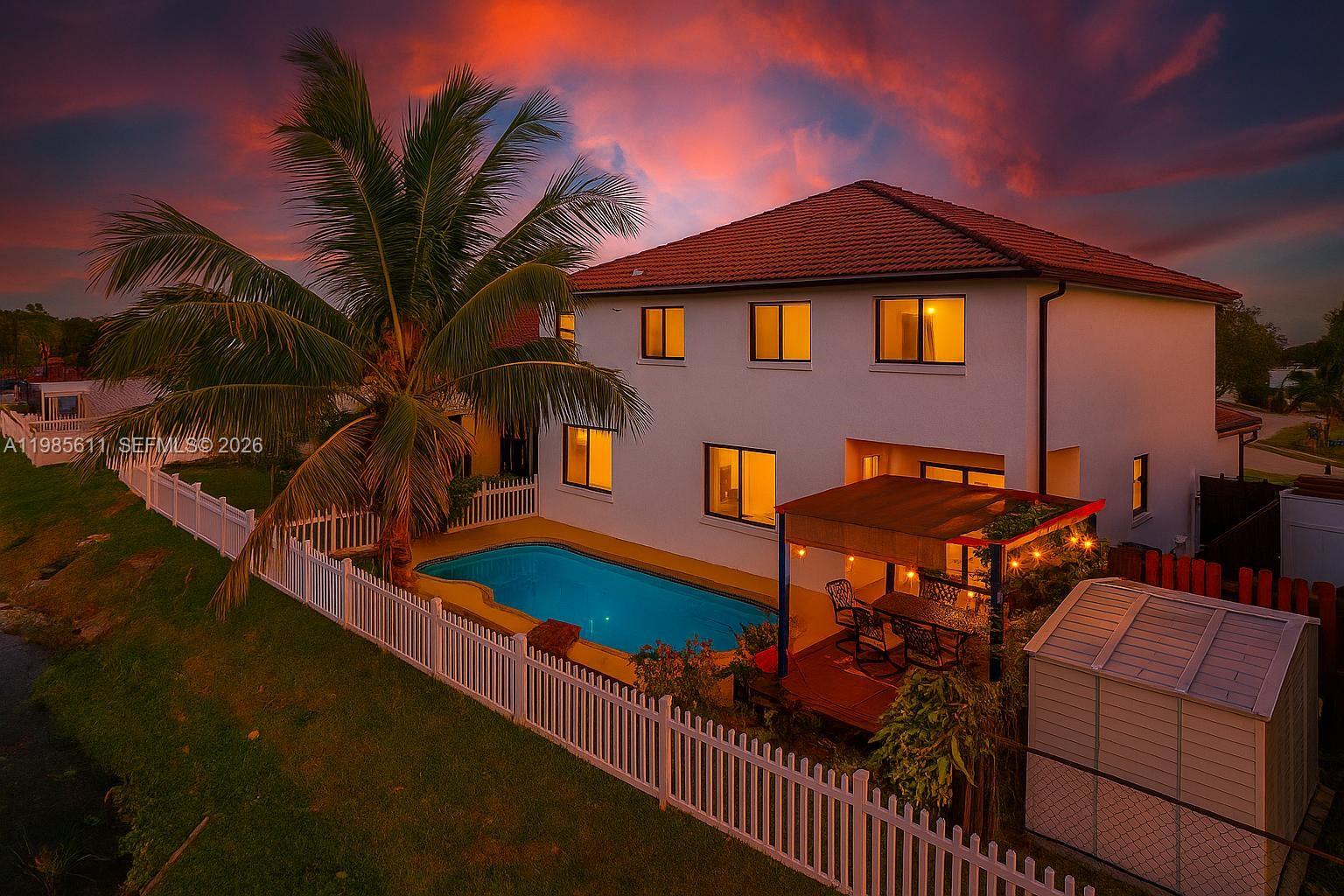 An aerial view of a two-story house with a pool, patio, and white fence at sunset — 22542 SW 103rd Ct, Cutler Bay FL 33190, CUTLER BAY, FL