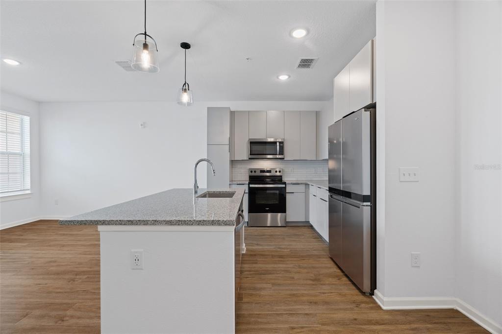 A modern kitchen features a granite-topped island, stainless steel appliances, and light-colored cabinetry — 1700 RANCH ROAD UNIT A4-7106, NOKOMIS, FL