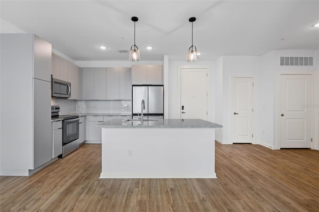 A modern kitchen features light gray cabinetry, stainless steel appliances, and a central granite island — 1700 RANCH ROAD UNIT A4-7106, NOKOMIS, FL