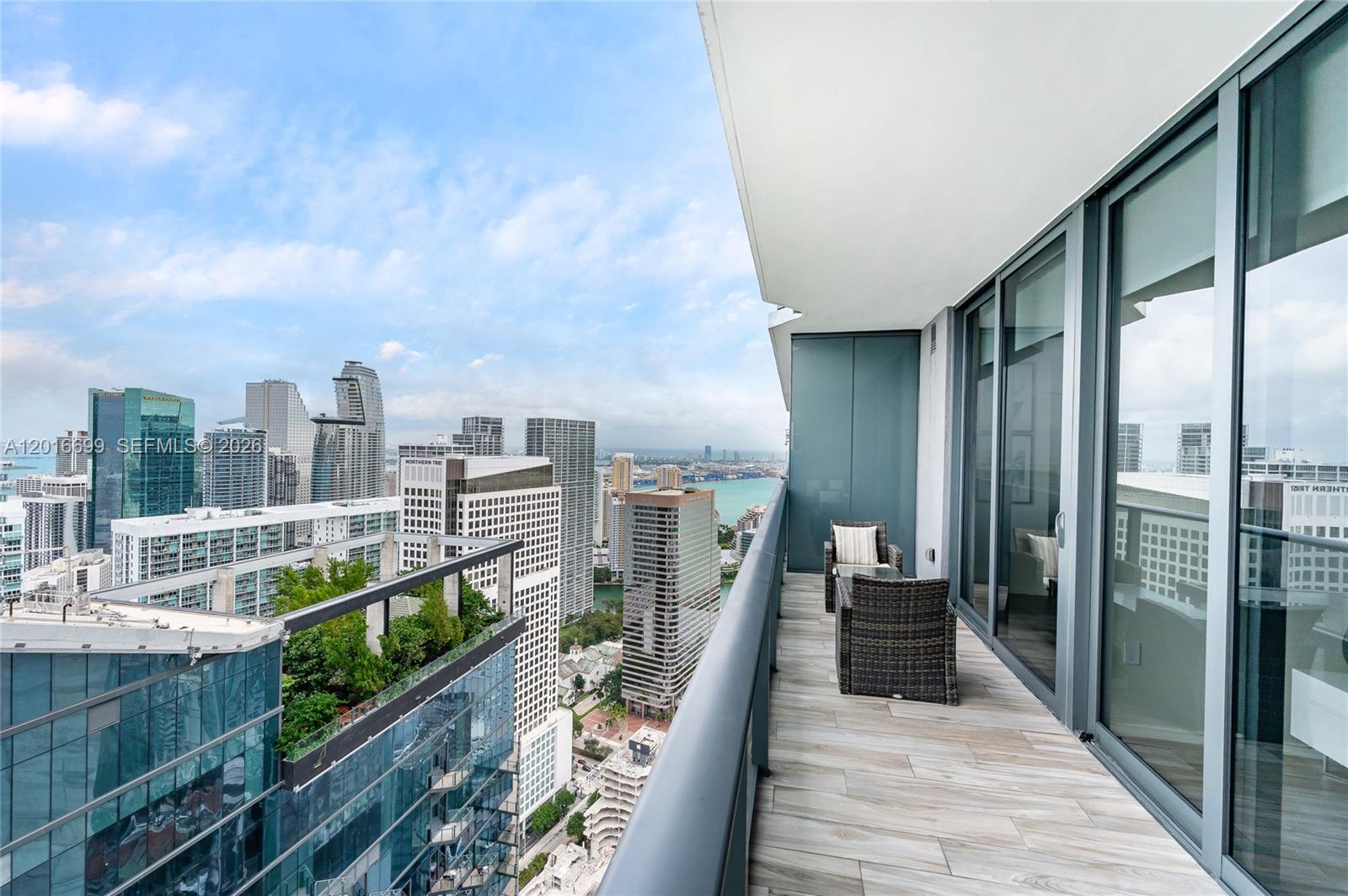 A high-rise balcony features wood-look tile flooring, outdoor furniture, and a panoramic city skyline view — 801 S Miami Ave # 5207, Miami FL 33130, MIAMI, FL