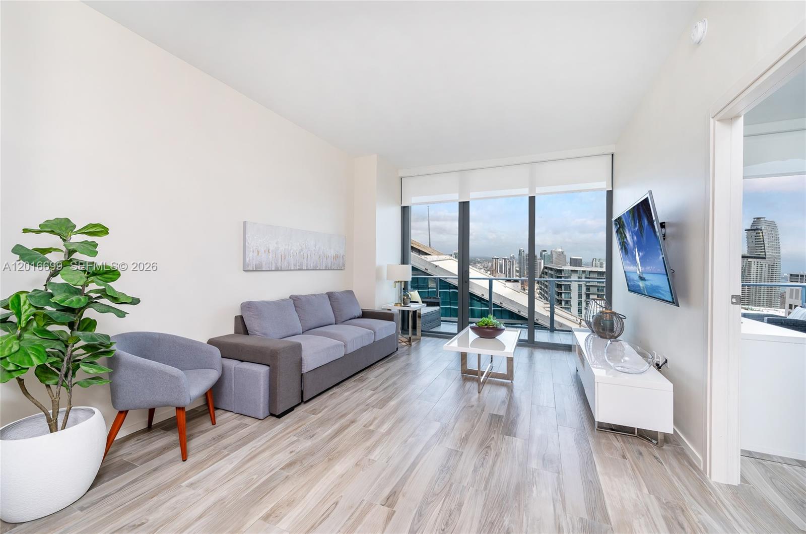 A modern living room features a grey sofa, armchair, white coffee table, and floor-to-ceiling windows — 801 S Miami Ave # 5207, Miami FL 33130, MIAMI, FL