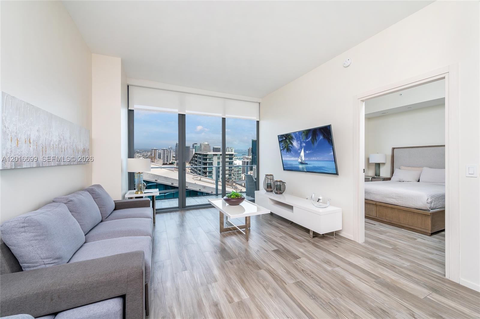 A living room with a grey sofa, white media console, and floor-to-ceiling windows overlooking cityscapes — 801 S Miami Ave # 5207, Miami FL 33130, MIAMI, FL