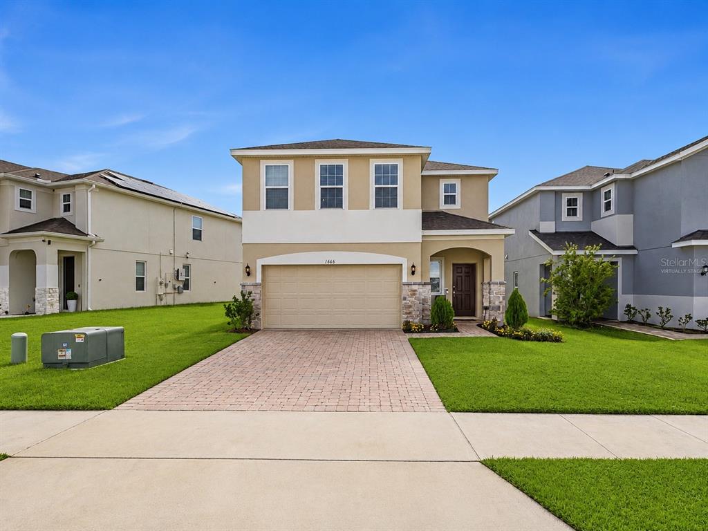 A two-story suburban house with a beige stucco exterior, stone accents, and a paved driveway — 1466 WOODMONT BOULEVARD, KISSIMMEE, FL
