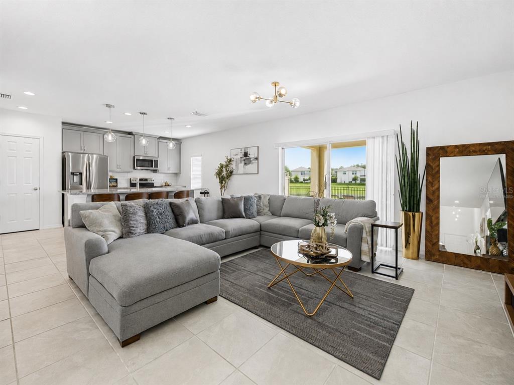 A living room with a gray sectional sofa, a round coffee table, and an open kitchen — 1466 WOODMONT BOULEVARD, KISSIMMEE, FL
