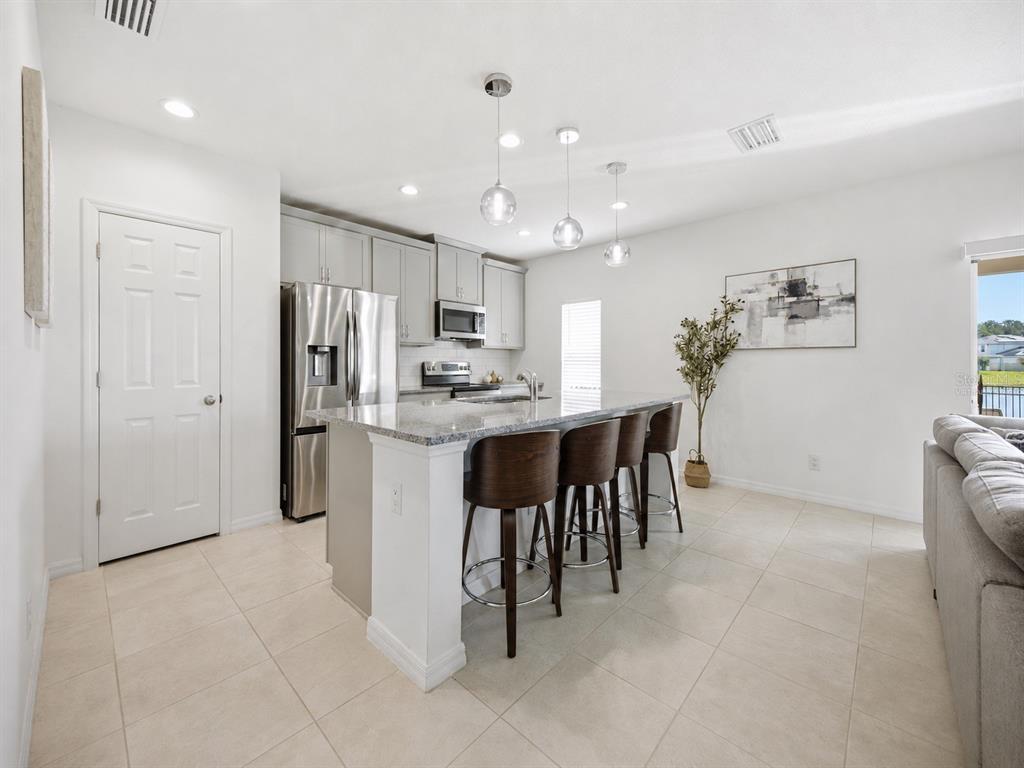 A kitchen with gray cabinets, stainless steel appliances, a granite island, and four bar stools — 1466 WOODMONT BOULEVARD, KISSIMMEE, FL