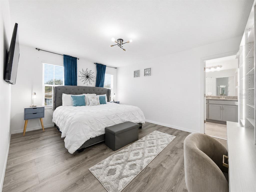 A bedroom features a gray upholstered bed, wood-look flooring, and an attached bathroom — 1466 WOODMONT BOULEVARD, KISSIMMEE, FL
