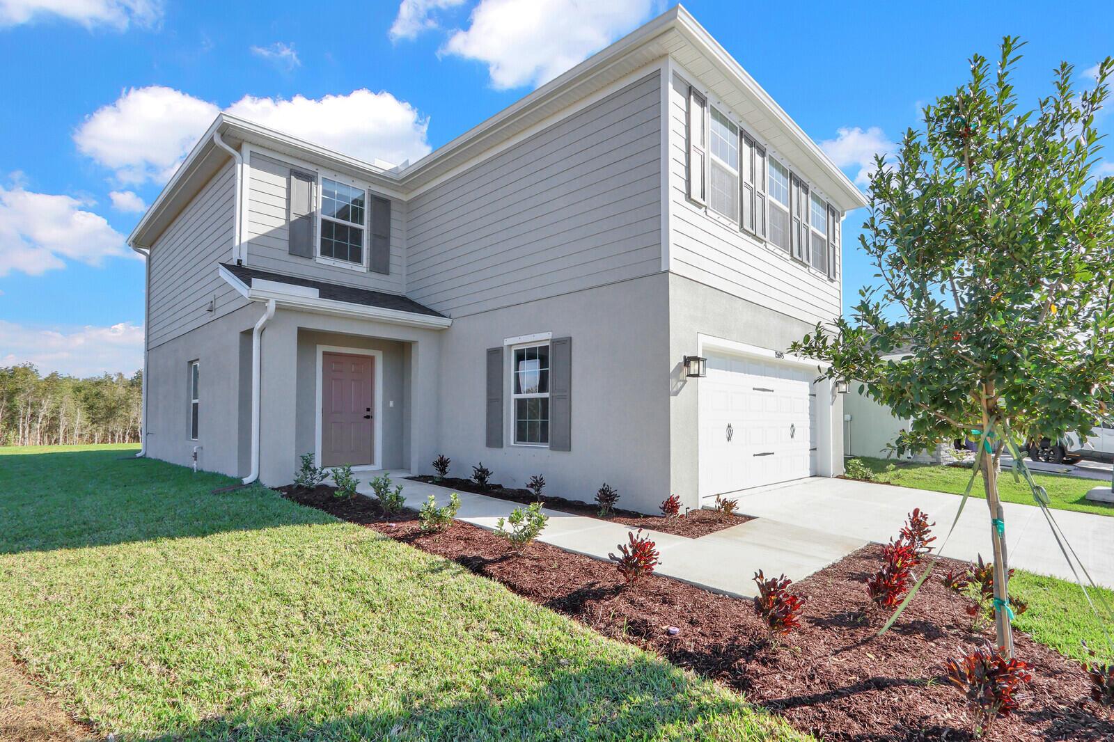A two-story house with gray siding and stucco features a front porch and garage — 15693 SW Twilight Street, FL 34956, FL