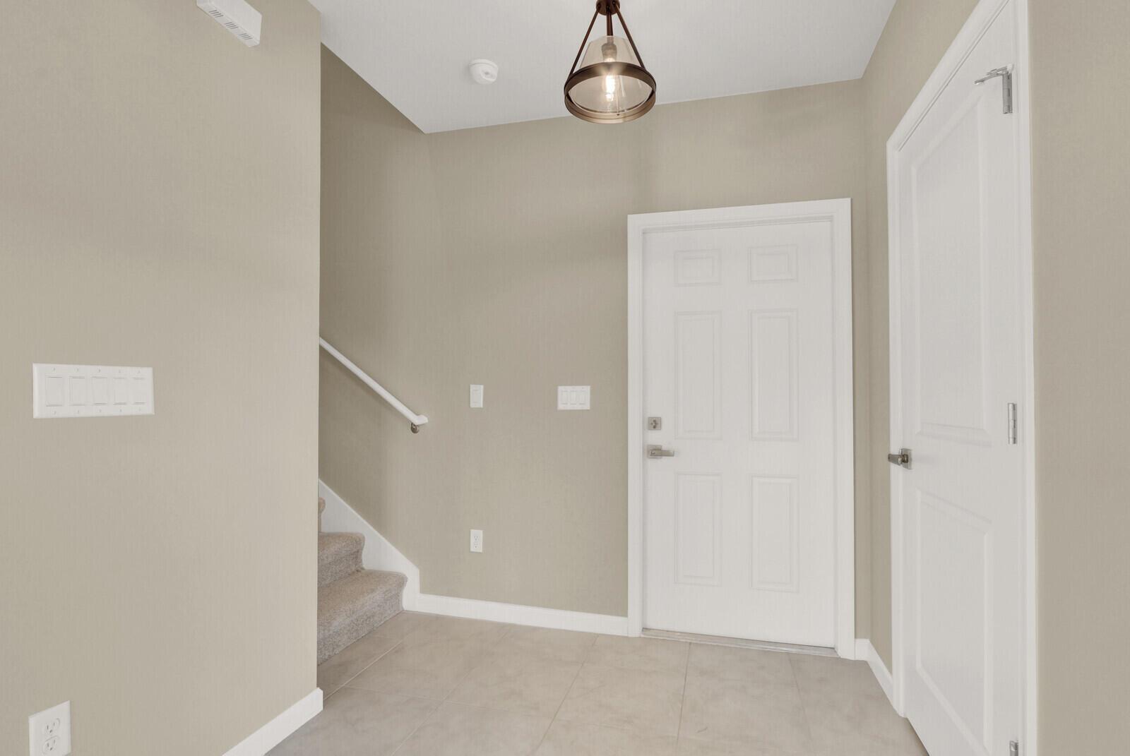 An entryway features beige walls, tile flooring, a staircase, and a white front door — 15693 SW Twilight Street, FL 34956, FL