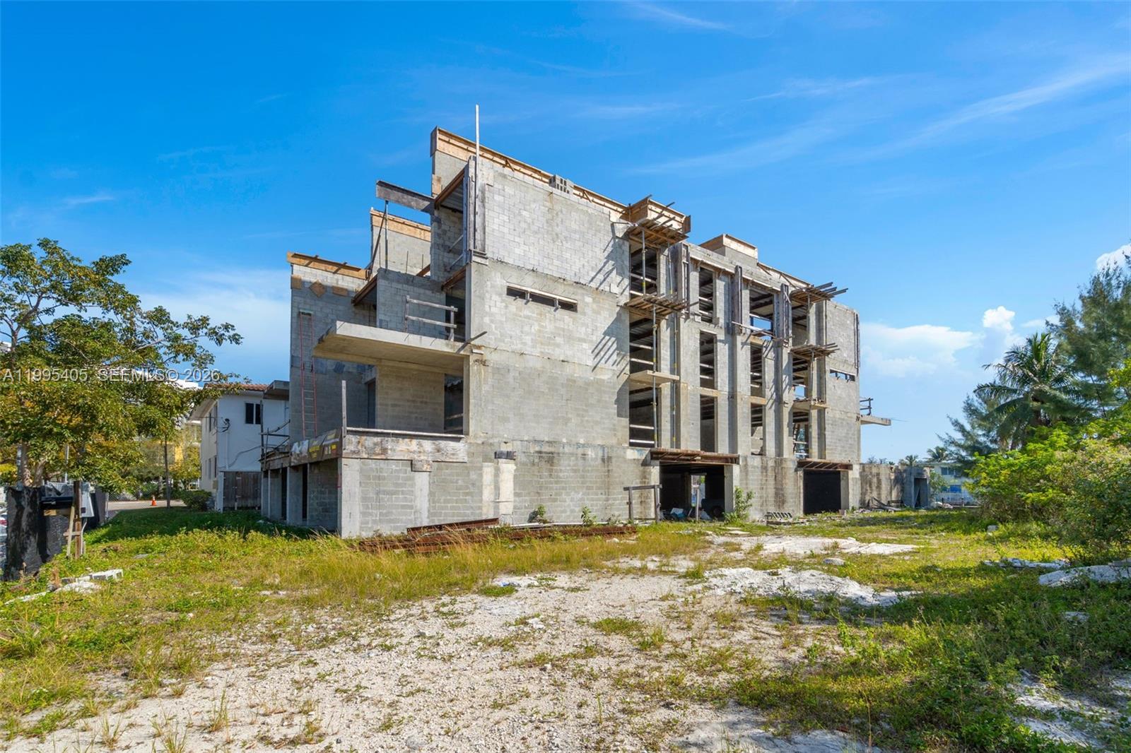 An unfinished multi-story concrete building stands on a dirt lot under a clear blue sky — 10 S Shore Dr, Miami Beach FL 33141, MIAMI BEACH, FL