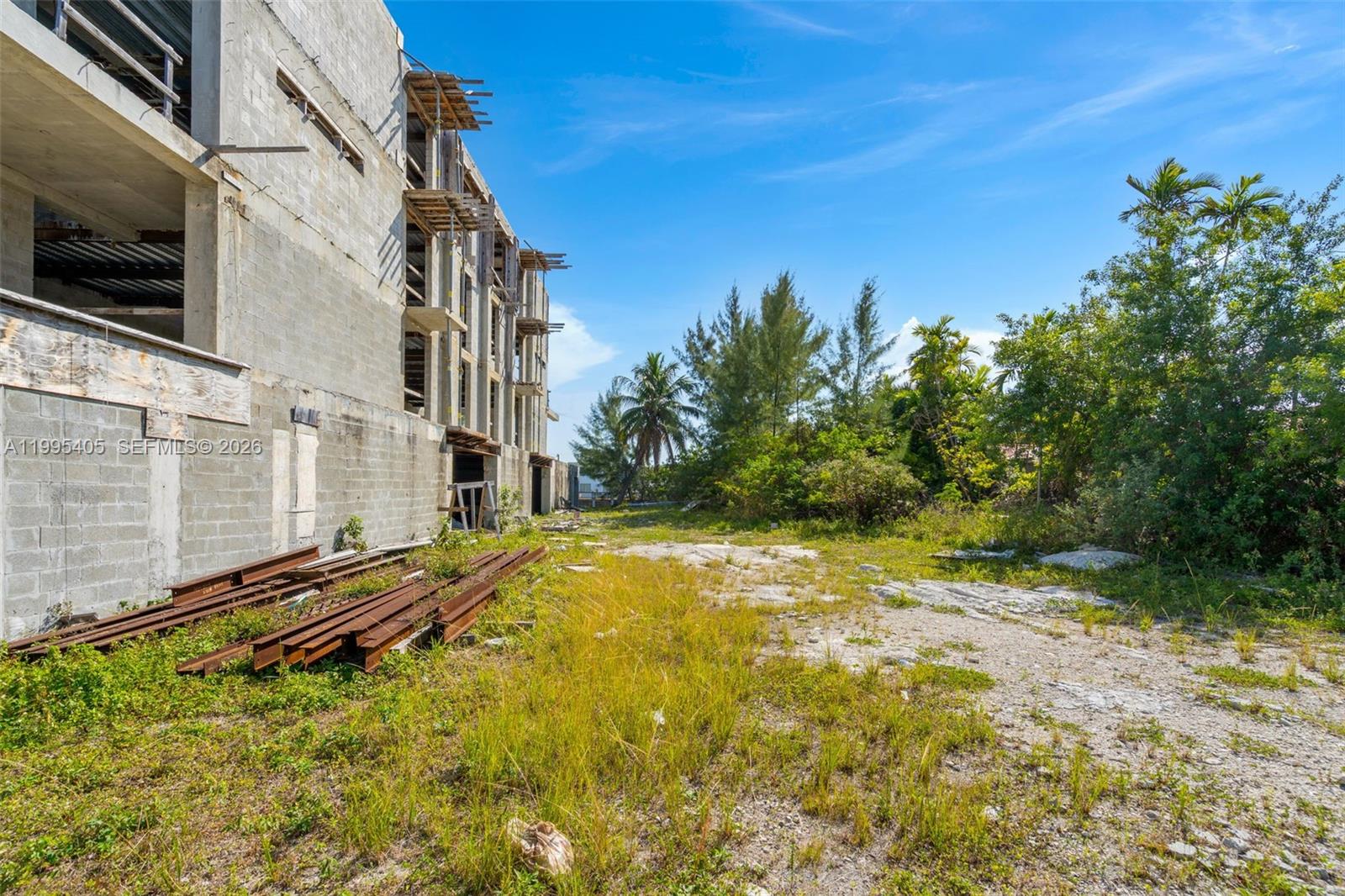 An unfinished concrete building stands next to a vacant, overgrown lot with scattered metal beams — 10 S Shore Dr, Miami Beach FL 33141, MIAMI BEACH, FL