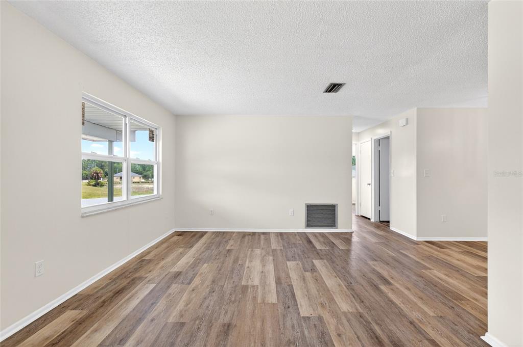 An empty living room features light-colored walls, wood-look flooring, a large window, and a vent — 1766 W GARDENIA DRIVE, CITRUS SPRINGS, FL