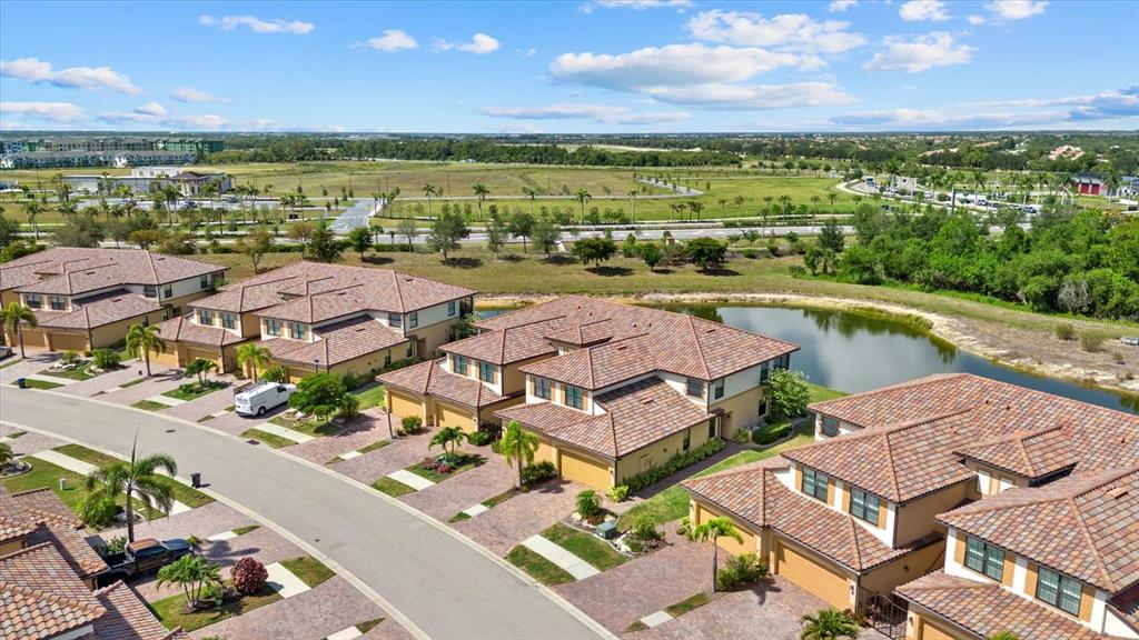 An aerial view shows several multi-story townhomes with tiled roofs situated near a small pond — 20080 RAGAZZA CIRCLE UNIT 102, VENICE, FL