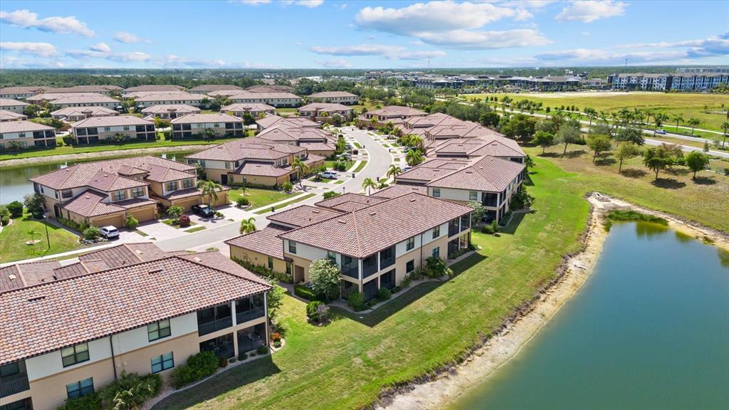 An aerial view shows multiple multi-story residential buildings with tile roofs near a small lake — 20080 RAGAZZA CIRCLE UNIT 102, VENICE, FL