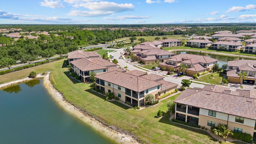 An aerial view shows multiple multi-story residential buildings with tile roofs situated near a pond — 20080 RAGAZZA CIRCLE UNIT 102, VENICE, FL