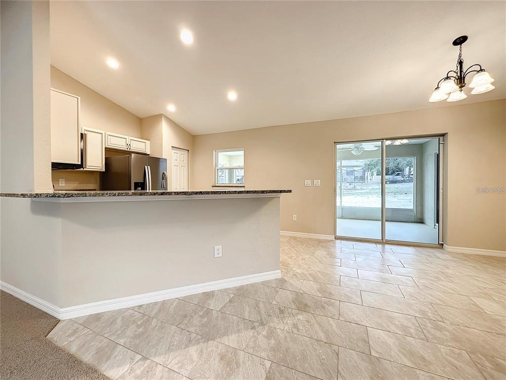 A kitchen with a breakfast bar and tile flooring opens to a dining area with sliders — 4887 SW 159TH LANE ROAD, OCALA, FL