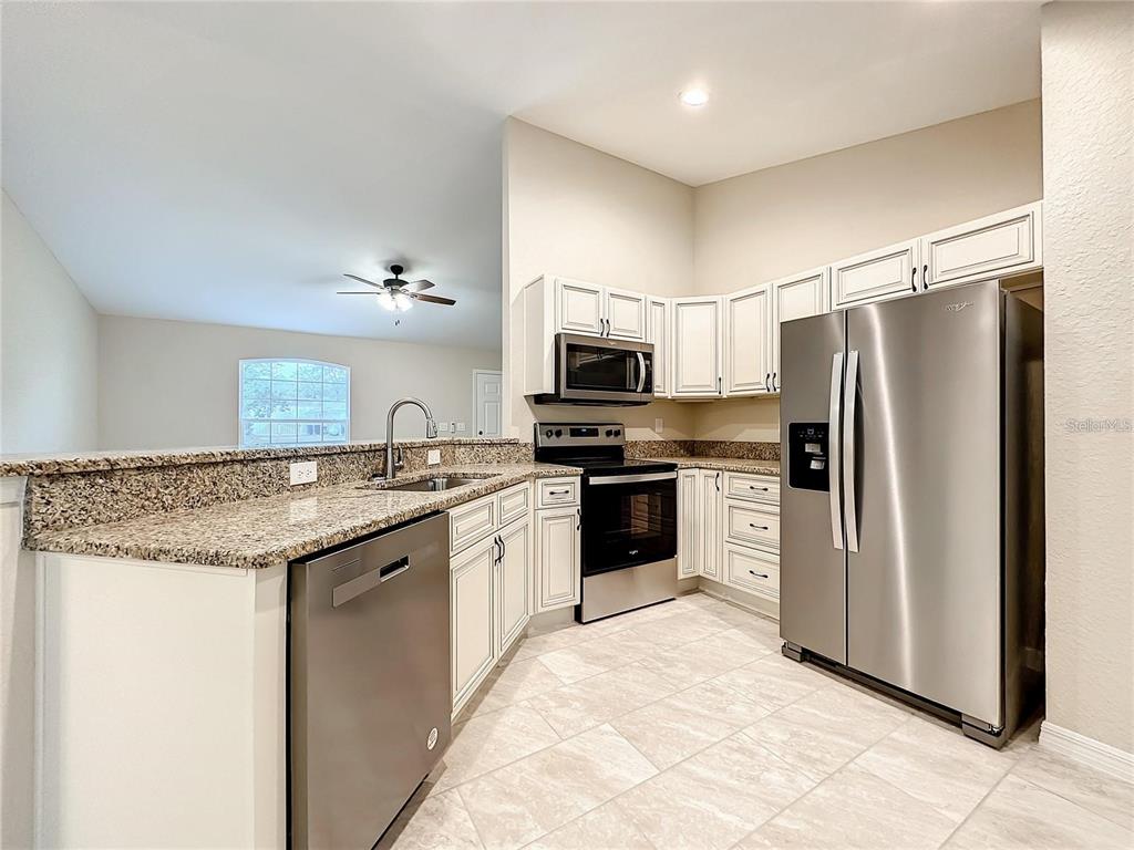 A kitchen features white cabinets, granite countertops, stainless steel appliances, and light tile flooring — 4887 SW 159TH LANE ROAD, OCALA, FL