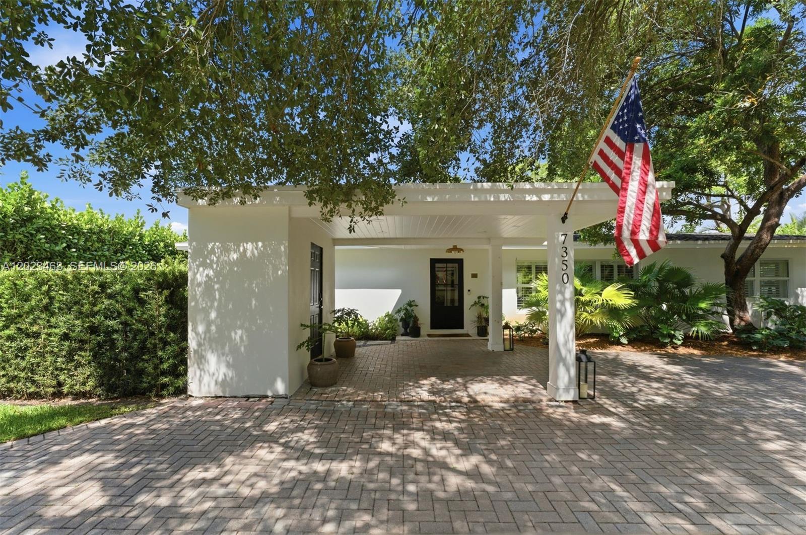 A white house exterior features a brick driveway, a covered entryway, and an American flag — 7350 SW 65th Ave, South Miami FL 33143, SOUTH MIAMI, FL