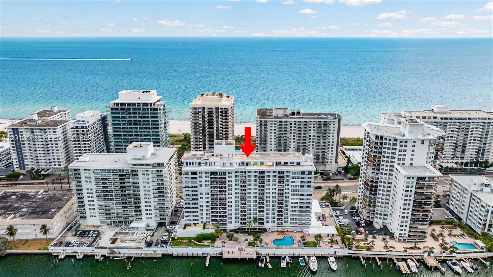 An aerial view shows a white high-rise residential building with a red arrow pointing downward — 5700 Collins Ave # 7J, Miami Beach FL 33140, MIAMI BEACH, FL