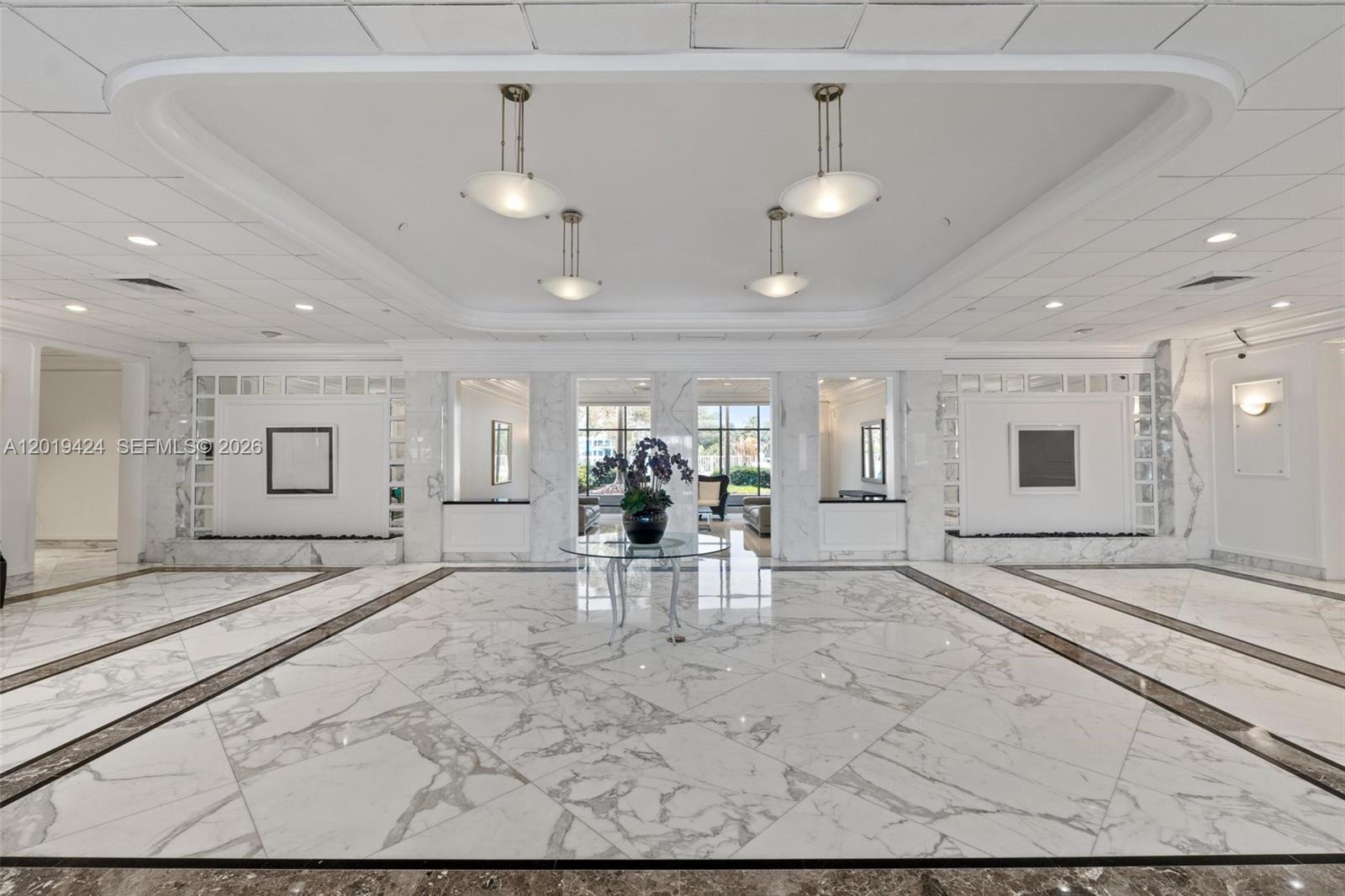 A spacious lobby features white marble floors, recessed lighting, and a central glass-topped table — 5700 Collins Ave # 7J, Miami Beach FL 33140, MIAMI BEACH, FL