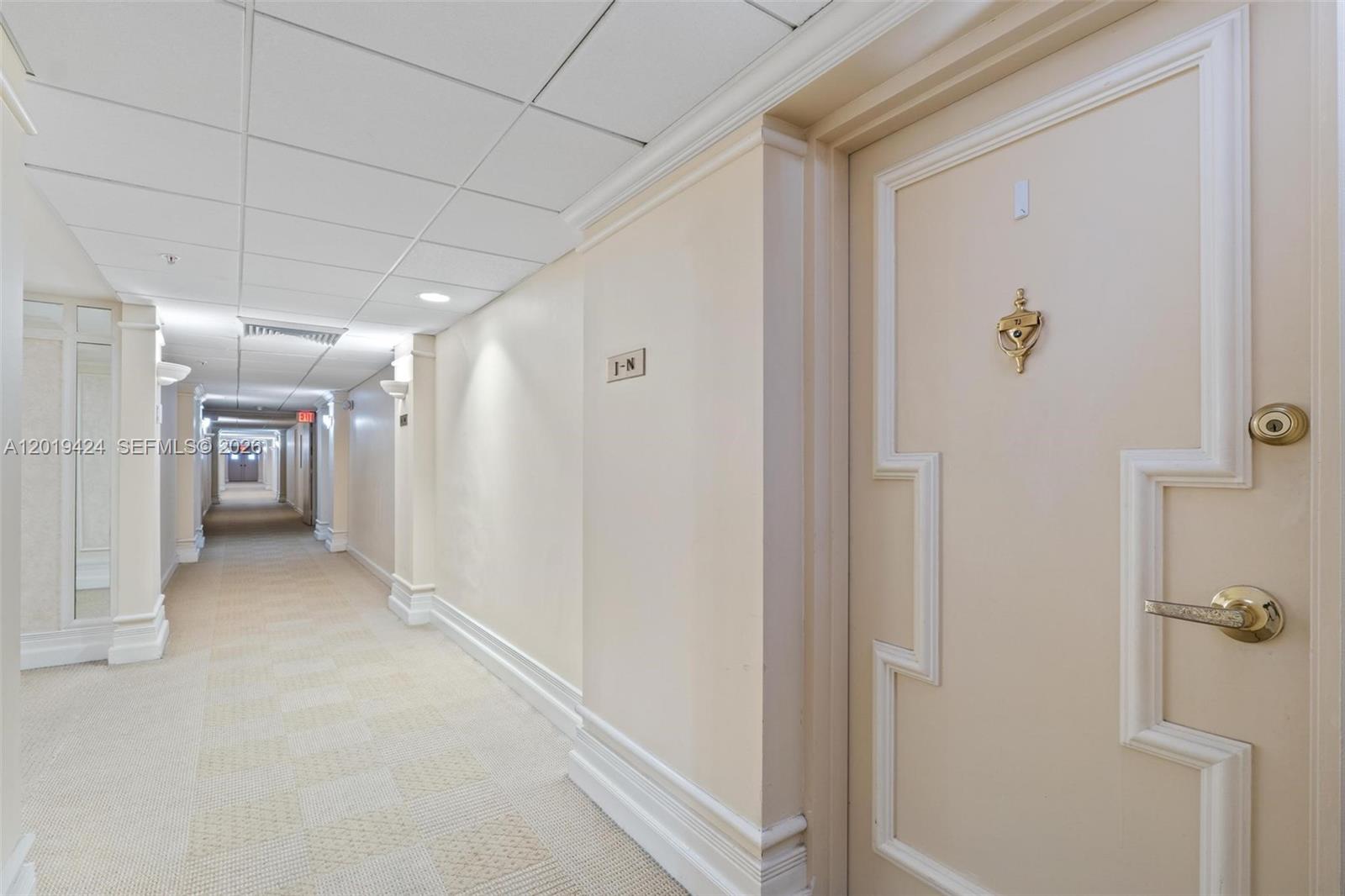 A long, carpeted hallway features a cream-colored door with a brass knocker and handle — 5700 Collins Ave # 7J, Miami Beach FL 33140, MIAMI BEACH, FL