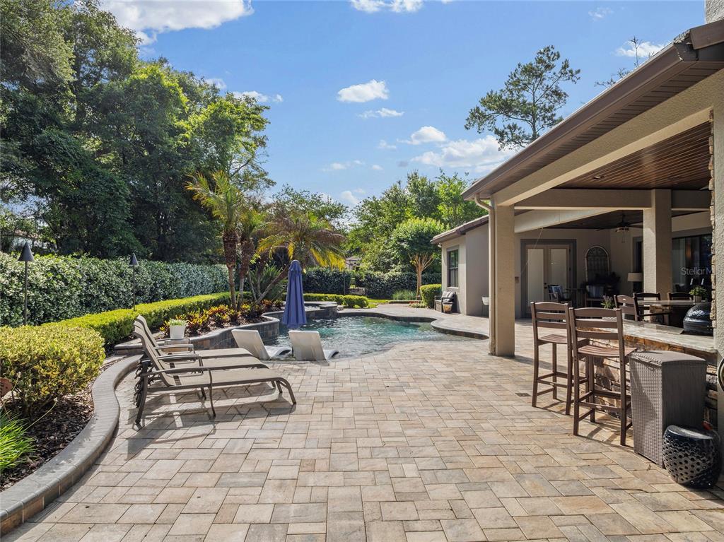 A backyard patio features a swimming pool, lounge chairs, and a covered outdoor kitchen area — 2238 SOARING EAGLE PLACE, LAKE MARY, FL