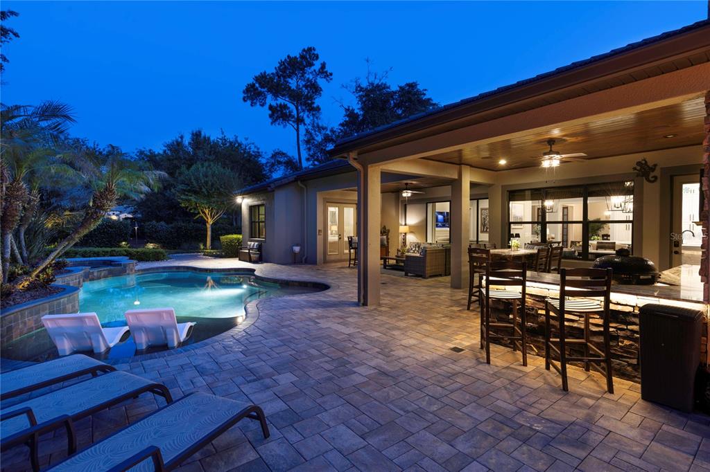 A covered patio with an outdoor kitchen and bar overlooks a swimming pool at dusk — 2238 SOARING EAGLE PLACE, LAKE MARY, FL