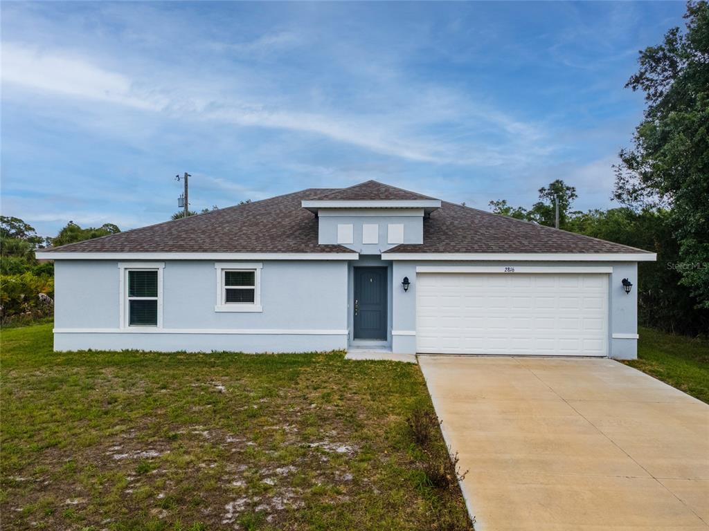 A light blue single-story house features a dark gray front door and a white garage — 4127 CONUS AVENUE, NORTH PORT, FL