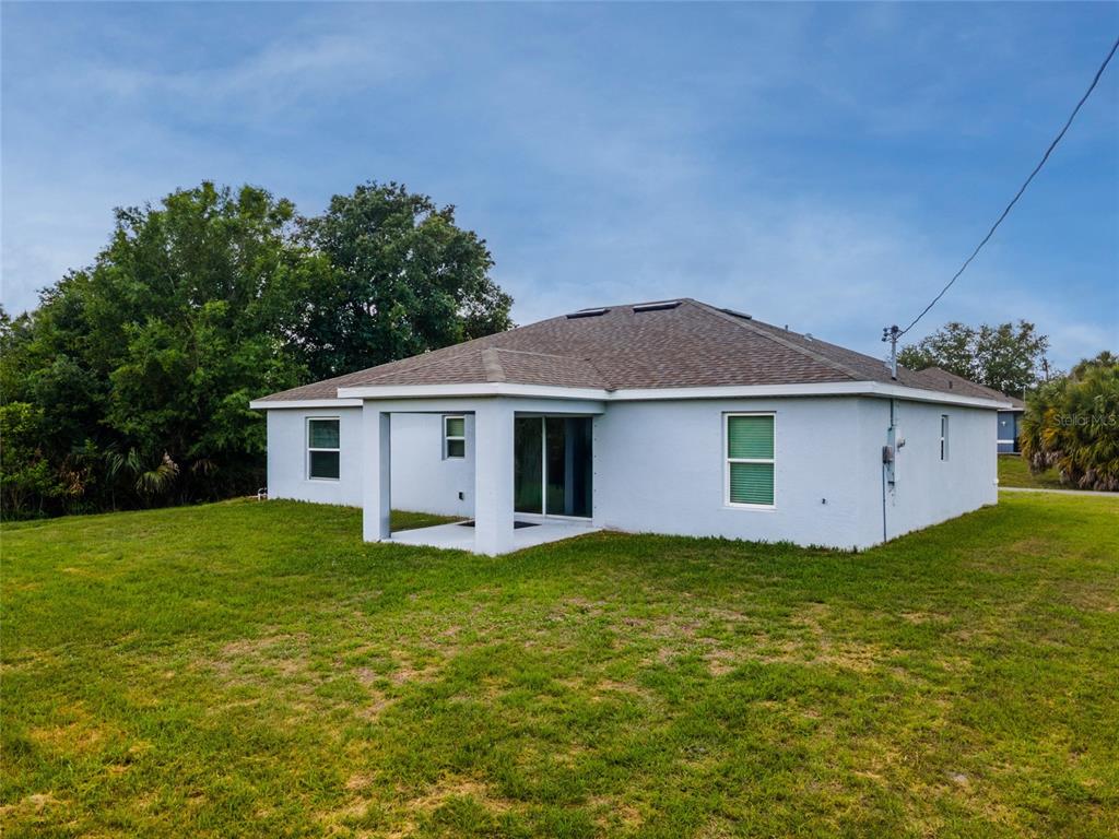 The rear exterior of a single-story house features a covered patio and a grassy yard — 4127 CONUS AVENUE, NORTH PORT, FL