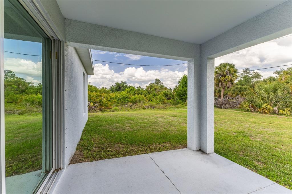 A covered concrete patio overlooks a grassy backyard with trees and a cloudy sky — 4127 CONUS AVENUE, NORTH PORT, FL