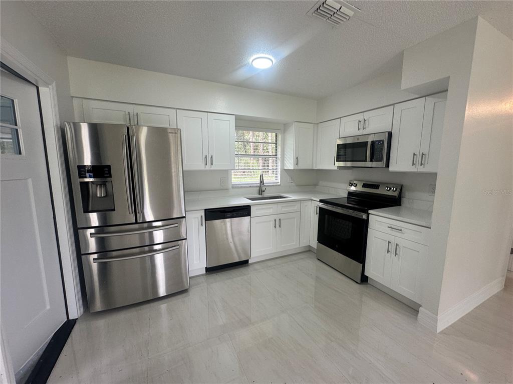 An open-concept kitchen and living area features white cabinets, stainless steel appliances, and tile flooring — 25527 ANTLER STREET, CHRISTMAS, FL