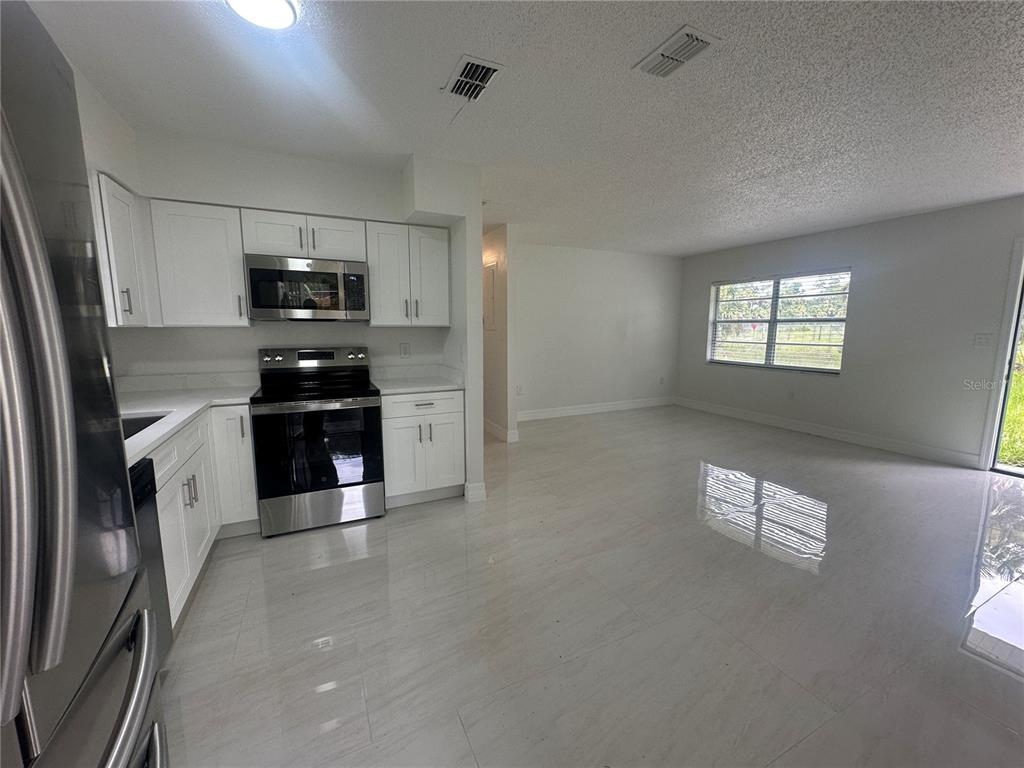 A kitchen features white cabinets, stainless steel appliances, and light-colored tile flooring — 25527 ANTLER STREET, CHRISTMAS, FL