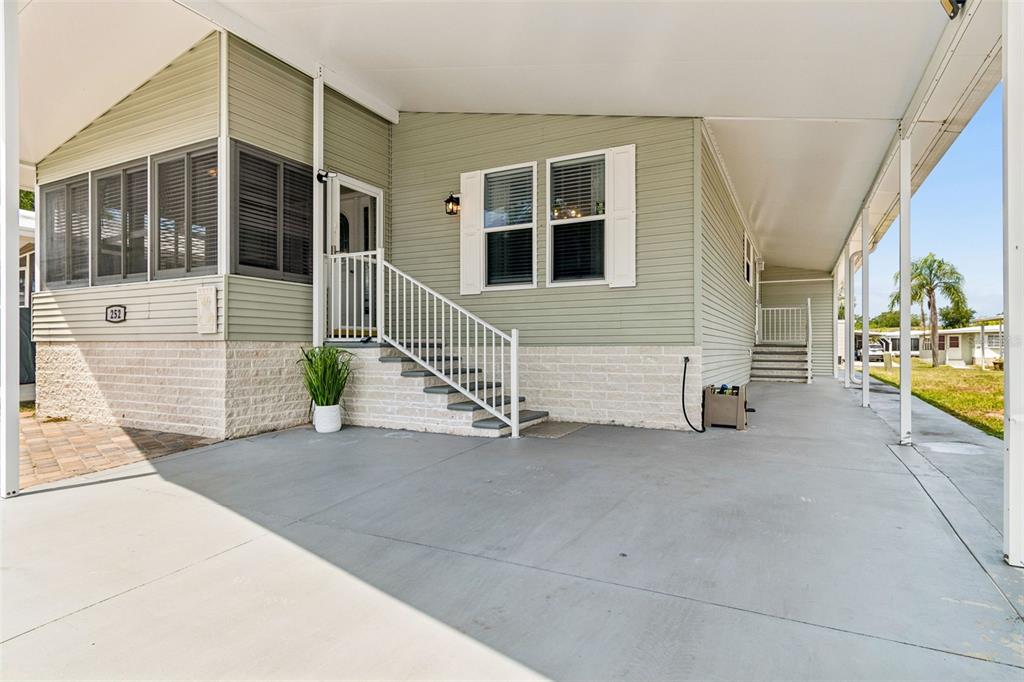 A light green manufactured home features a concrete carport, white railings, and brick skirting — 9790 66TH STREET N UNIT 252, PINELLAS PARK, FL